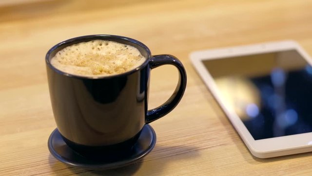 Digital tablet and cup of coffee on wooden desk. Simple workspace or coffee break in morning.