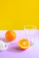Oranges, a transparent glass and a juicer. Bright background, creative frame, fashion light. Vertical frame, purple and yellow.