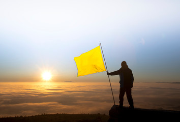 silhouette of successful man waving yellow flag at the summit