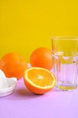 Oranges, a transparent glass and a juicer. Bright background, creative frame, fashion light. Vertical frame, purple and yellow.