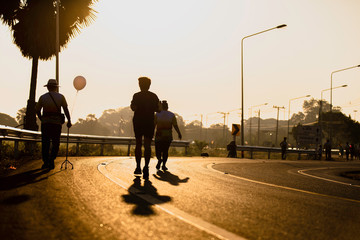 Silhouette of old Man with walking stick laying  and jogging walking people on road against sunset for exercise.Staff cane three legs .