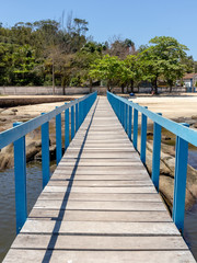 Naklejka premium Long wooden pier over rocks on the way to the coast with trees in the background, Paqueta Island, Rio de Janeiro, Brazil