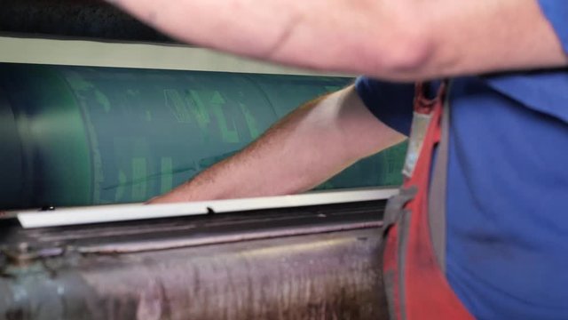 Worker installs new printing plates at the ink rollers of press machine