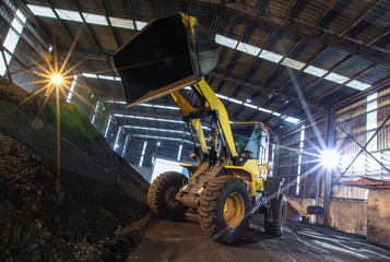 Heavy wheel loader excavator machine loading sand at quarry in a warehouse.