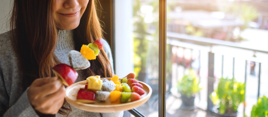 Closeup image of an asian woman holding and eating a fresh mixed fruits on skewers