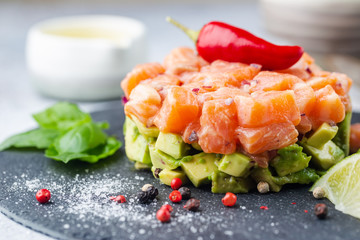 Delicious avocado and raw salmon salad, tartare, served on a black plate with lime, light background