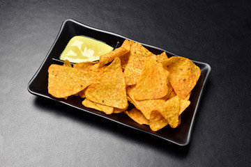 nachos chips with cheese dipping in black plate on dark background