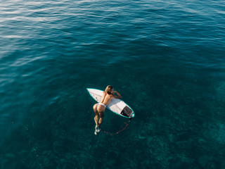 Aerial view of attractive surfer woman relax with surfboard in tropical ocean. - obrazy, fototapety, plakaty