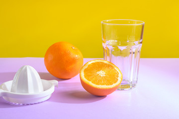 Oranges, a transparent glass and a juicer. Bright background, creative frame, fashion light.