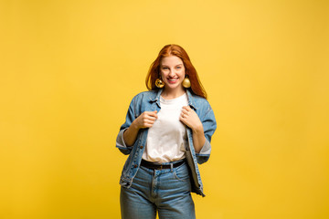 New Year's look. Caucasian woman's portrait on yellow studio background. Beautiful female red hair model in jeanse. Concept of human emotions, facial expression, sales, ad, winter mood, Christmas.