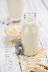Old wooden table with fresh Oat Milk (close-up shot; selective focus)