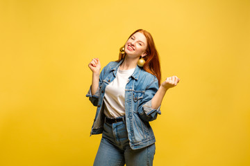 New Year's look. Caucasian woman's portrait on yellow studio background. Beautiful female red hair model in jeanse. Concept of human emotions, facial expression, sales, ad, winter mood, Christmas.