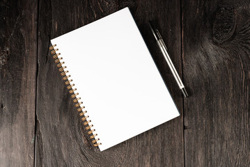 business concept, a notebook for notes with a white sheet and a black pen on a rustic wooden dark brown table