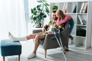 caring woman sitting near cheerful and injured boyfriend