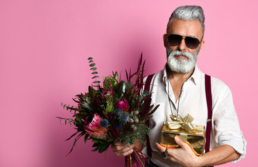 Stylish middle-aged bearded man with a modern haircut, sunglasses and fashionably dressed holds a...