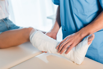 cropped view of orthopedist touching fractured leg of woman