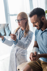 Obraz premium attractive orthopedist in glasses holding x-ray near injured man suffering from pain