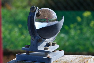 Weather station and the sun in a blue sky reflected in the glass sphere of a beautiful heliograph on a green background