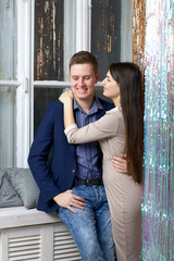 A young man hugs his wife. She hugs his neck. Near Shining rain curtain.