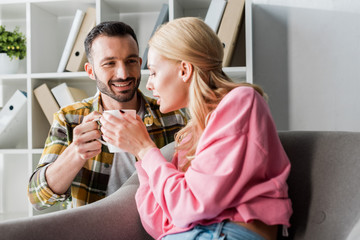 positive man giving cup of tea to woman at home