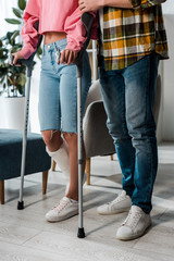 cropped view of injured woman holding crutches while standing with man at home