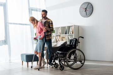 wheelchair near injured woman holding crutches while standing with man