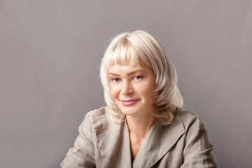 Fototapeta premium Portrait of older business woman smiling by grey wall.