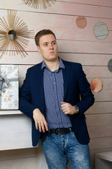 The young man rests his elbow on a shelf. He looks away thoughtfully.