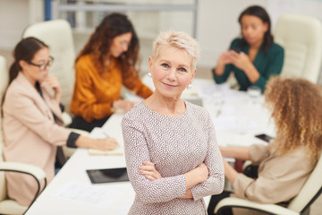 Confident mature woman standing with arms closed looking at camera smiling with colleagues...