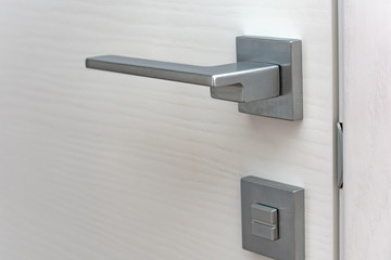 Modern chrome door handle and lock on white wooden door. Close-up elements of the modern interior of the apartment. Ajar white door.