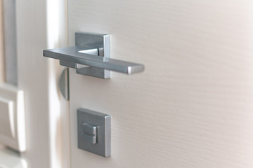 Modern chrome door handle and lock on white wooden door. Close-up elements of the modern interior of the apartment. Ajar white door.