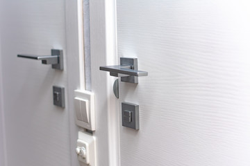 Modern chrome door handle and lock on white wooden door. Close-up elements of the modern interior of the apartment. Ajar white door.