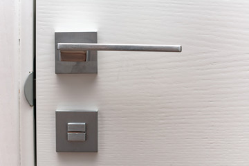 Modern chrome door handle and lock on white wooden door. Close-up elements of the modern interior of the apartment. Ajar white door.