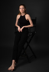 Fototapeta na wymiar Beautiful brunette model in black clothes sitting on chair while posing on dark studio background