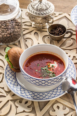 Obraz na płótnie Canvas Red beetroot soup borshch with bread bun and sour cream on oriental wooden table