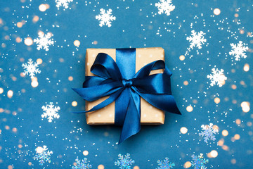 Attractive gift with blue ribbon on a blue background. Snow and lights. Merry Christmas, New Year, winter concept.