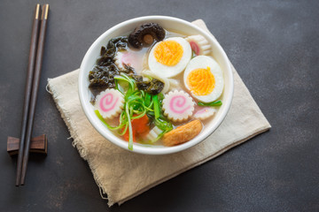 Fototapeta na wymiar Asian style soup with udon noodles with steam and smoke, pork, boiled eggs, mushrooms and green onions close-up in a bowl on old table. horizontal top view from above
