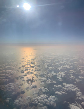 Sky travel. View from the illuminator. Fluffy white clouds. Sunlight pink and yellow reflexion on the water. Blue sky background.