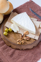 vertical photo, brie cheese next to lie nuts and olives on a wooden board next to fresh buns