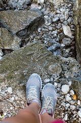 A woman on the edge of a rocky cliff in sneakers. View of female legs in sneakers