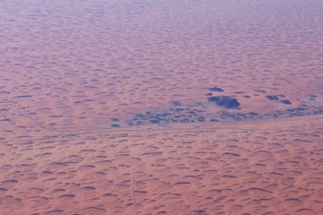 View from the air of round irrigation fields and farms surrounded by sand dunes in the desert in Saudi Arabia