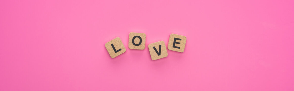 top view of love lettering on wooden cubes on pink background, panoramic shot