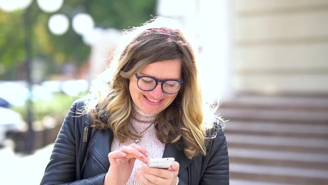 A beautiful girl with glasses standing and comunicate with help of smartphone. Smiling, good news