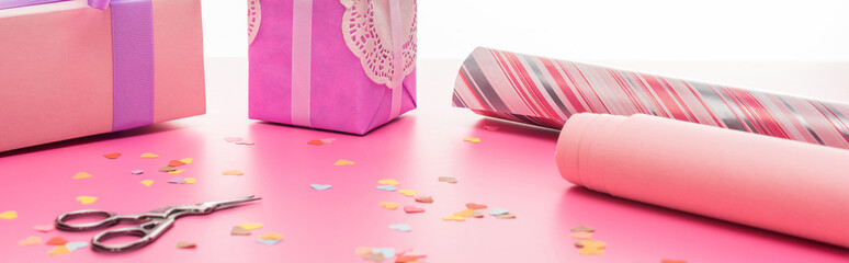 valentines confetti, scissors, wrapping paper, gift boxes on pink surface isolated on white, panoramic shot