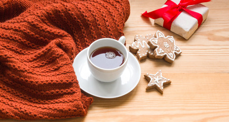 Knitted thing, a Cup and saucer with hot tea and gingerbread on a wooden background. The concept of warmth, comfort, winter evening.