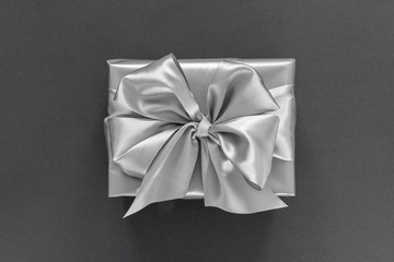 Festive background with silver gift, gift box with silver ribbon and bow on black background, flat lay, top view