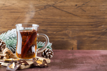 Winter hot tea with cinnamon, anise, chocolate with fruit, cone and christmas tree branch on wood brown background.