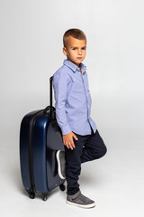 Happy young boy sitting behind black suitcase isolated over white background.