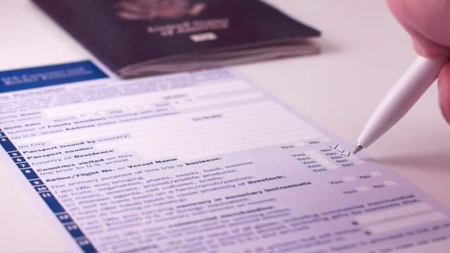 Man fills out a customs declaration form next to an American passport on a white background. Close-up