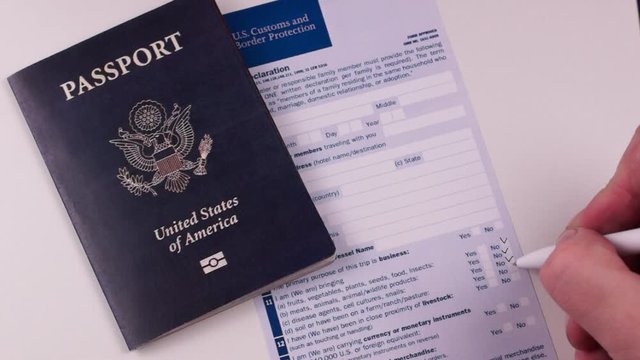 Man fills out a customs declaration form next to an American passport on a white background. Close-up